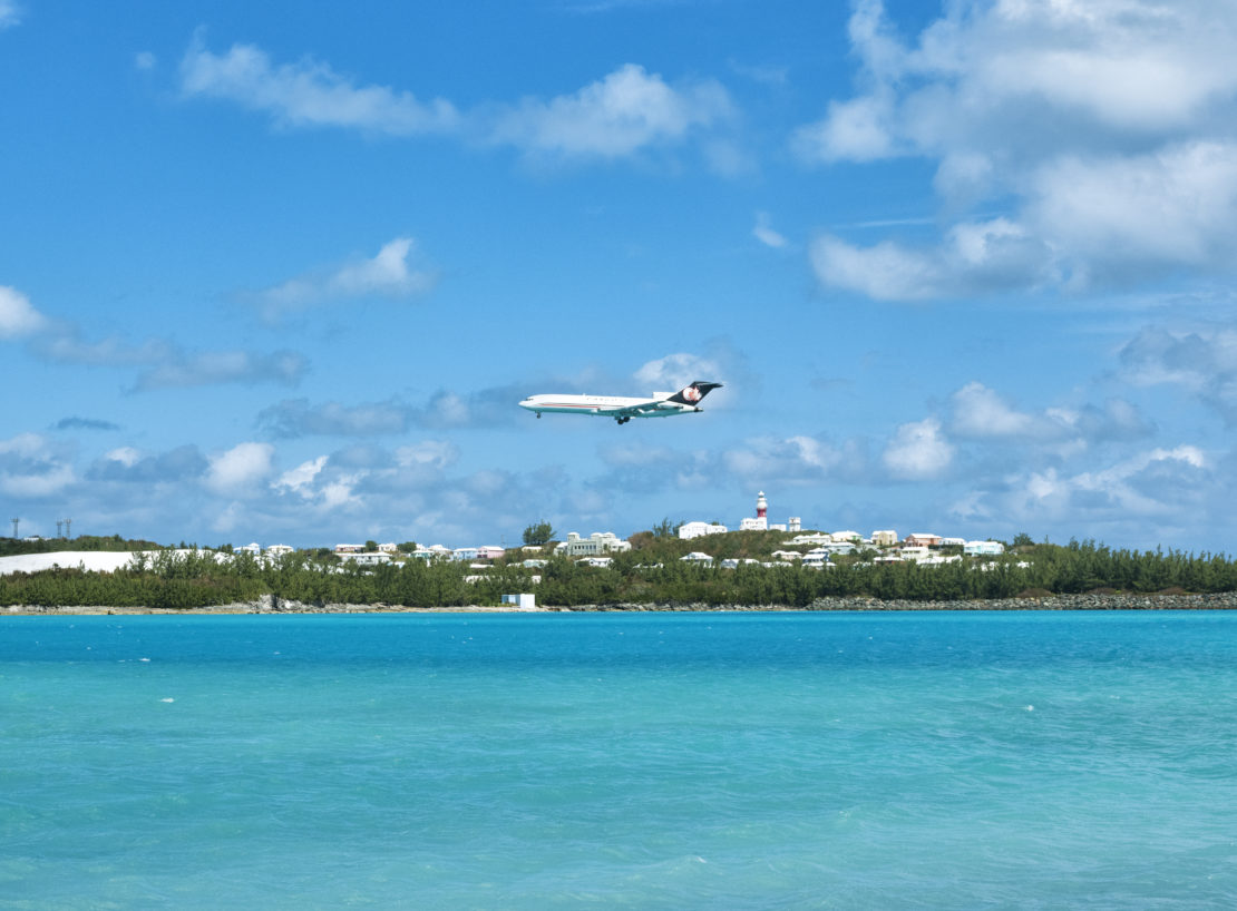 an airplane above clear water approaching the runway for landing